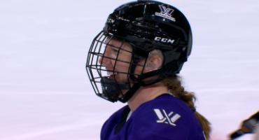 Grace Zumwinkle, while wearing a hockey helmet and in uniform, smiles during an ice hockey game.