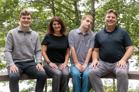 Dean Jamie Prenkert with his partner and two sons seated on a stone bridge in the woods.