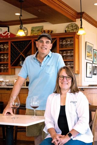 Mark and Pattie Bjornson posing at a table with two glasses of wine.