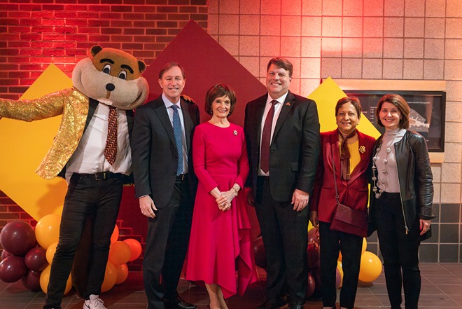 Carlson School leadership and Goldy Gopher posing before maroon and gold squares and balloons.