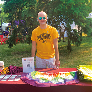 Alum, Jon Schroeder, smiles in front of the Carlson School's Pride table at the Twin Cities Pride Festival in July 2021.