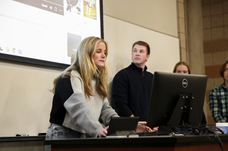 A student leaning setting up a presentation while teammates ready themselves before the screen.