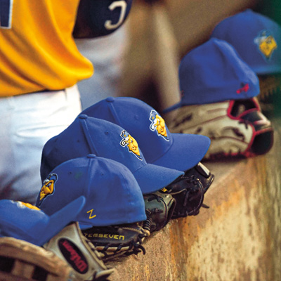 Baseball gloves with baseball caps sitting on top of them lay on top of a cement wall.