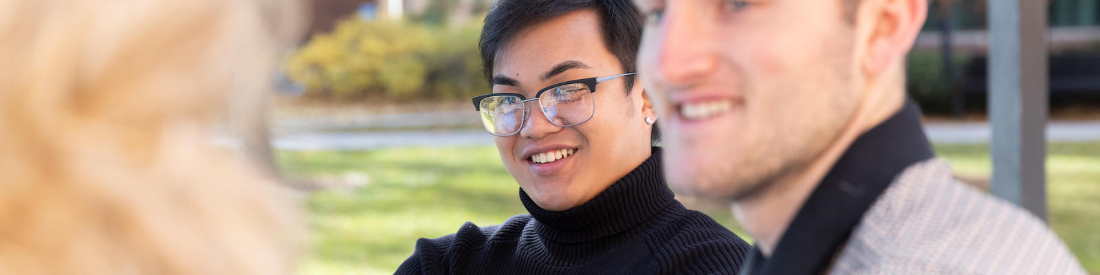 Student with glasses smiling in a small group of people talking.