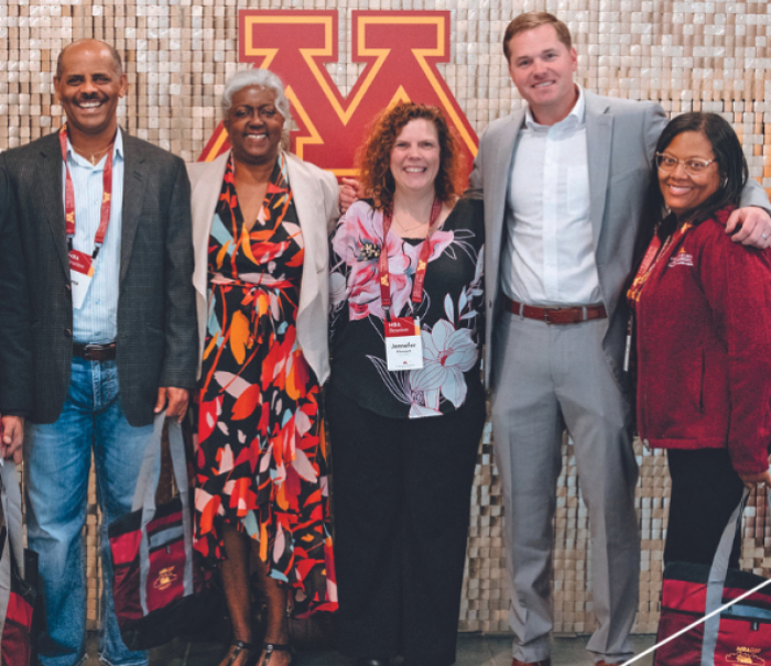 Group of MBA alumni posing in front of maroon and gold photo backdrop.