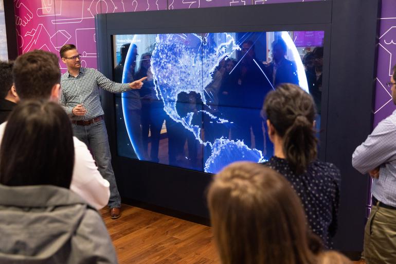 A person standing in front of a large screen with a large screen showing a map of the earth