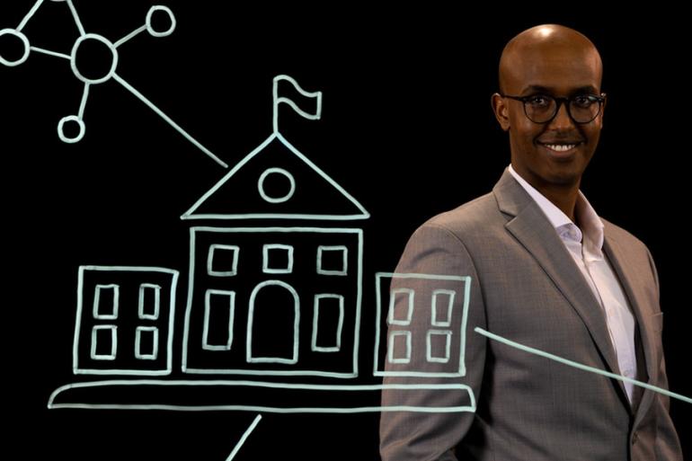 Abdifatah Ali stands behind an illustration of a university and networks.
