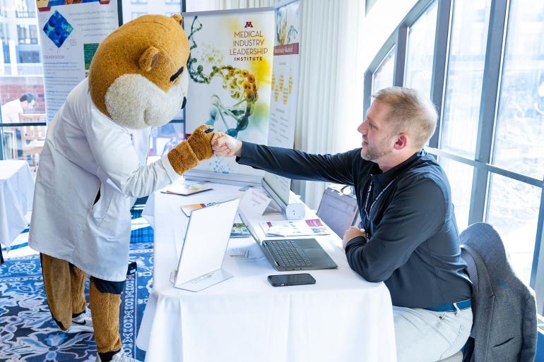 Goldy Gopher in lab jacket talking with person