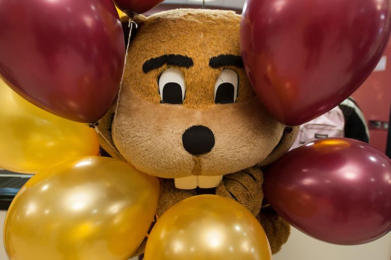 Goldy Gopher smiling to the camera through a bunch of balloons.
