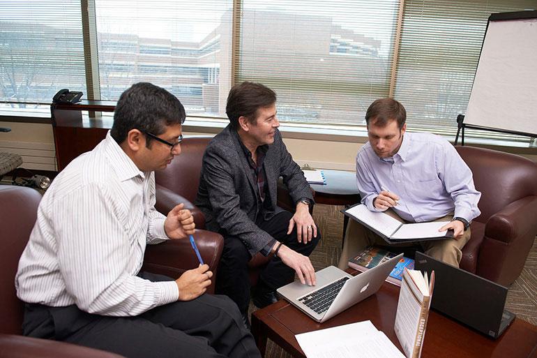 Men seated in front of laptop on desk discussing medical industry graduate certificate