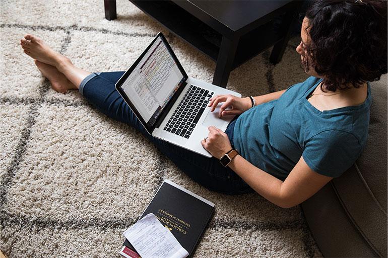 Woman sitting on floor working on Master of Business Administration homework on her laptop