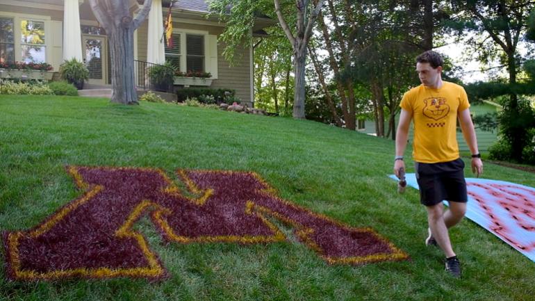 Keegan Masser paints the U of M logo on a lawn for YardLogo.