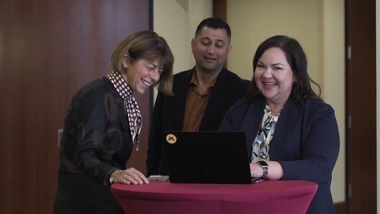 Three adult learners gathered around a laptop.