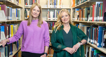 Connie Wanberg and Michelle Duffy stand in a library aisle by book shelves