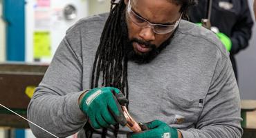 A man wearing safety glasses and gloves examines a pipe in a career readiness course.