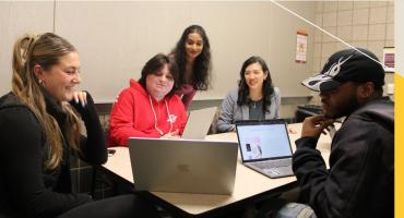 Students collaborate on a project while receiving feedback from a professor.
