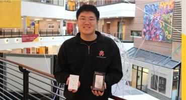 Leon Xue poses with an InvisOutlet and packaging in the Carlson School atrium.