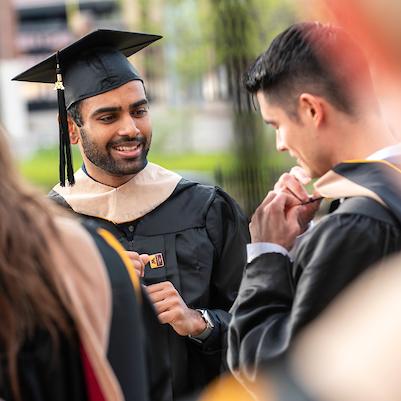 Graduate watching another fasten their hood during Commencement