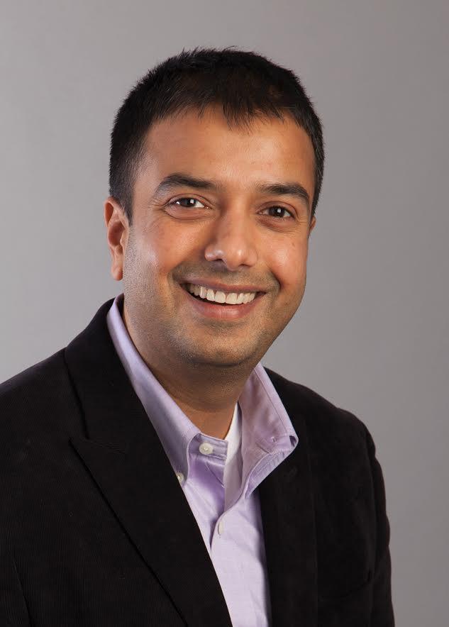 headshot of Rahul Koranne, smiling, and wearing a dark jacket over a light purple button up shirt with the collar unbuttoned and a white undershirt underneath