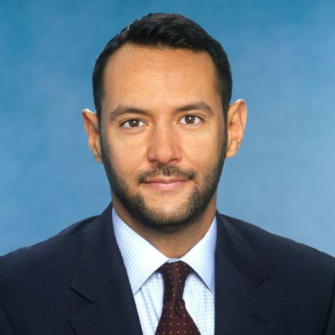 Photo of Yasser Boualam wearing a navy jacket, light blue collared shirt and maroon tie
