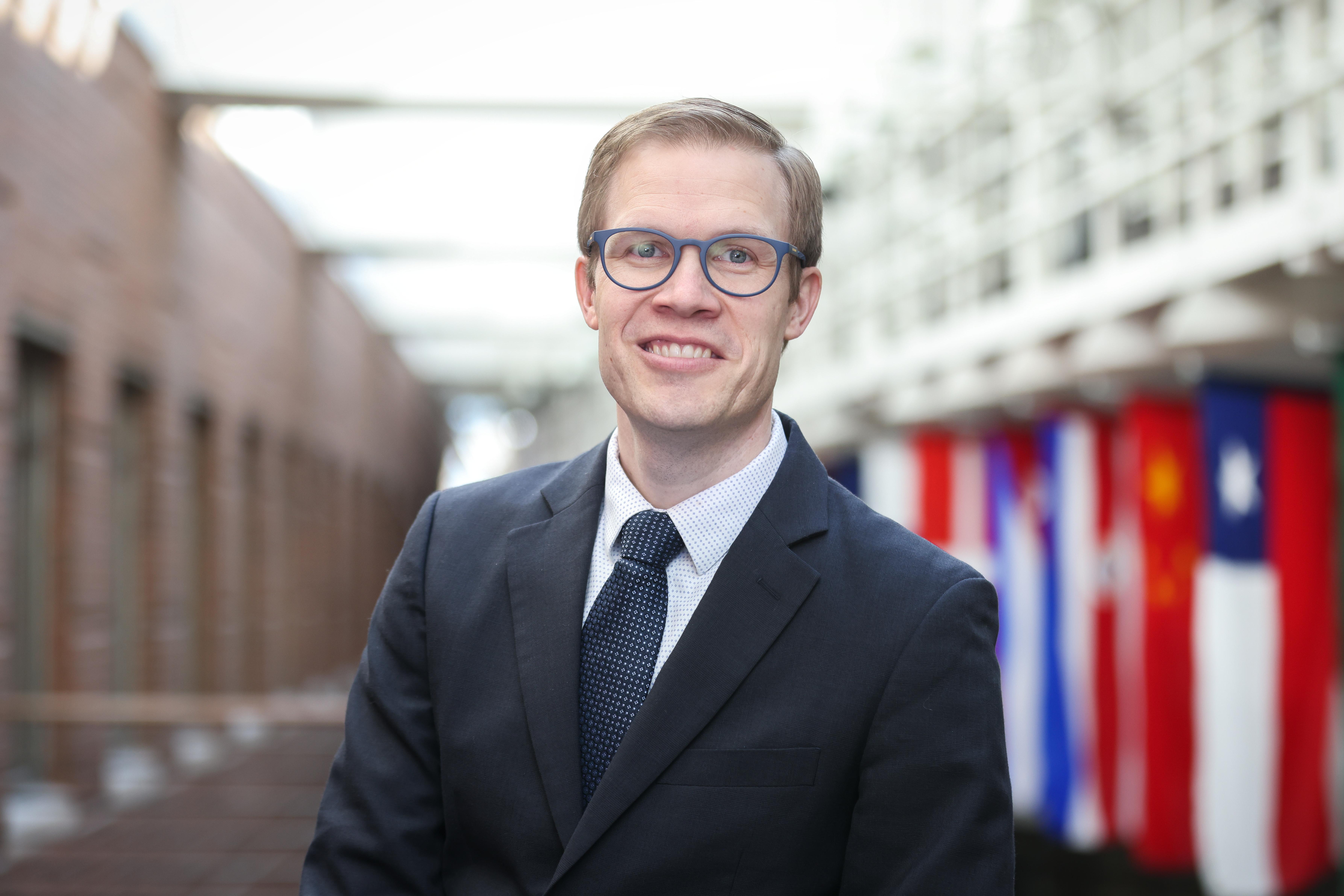 Headshot of Bryan Messerly in front of international flags hanging in the Carlson School of Management building.