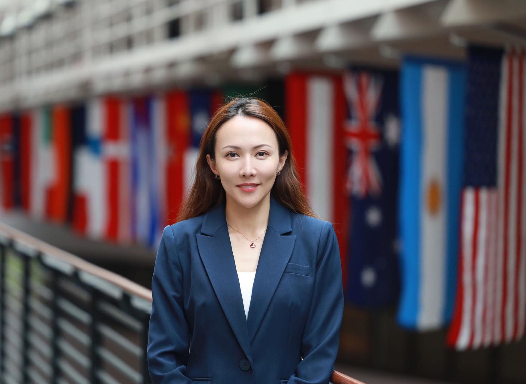Qian (Leah) Zhang Standing in front of international flags in Carlson School of Management
