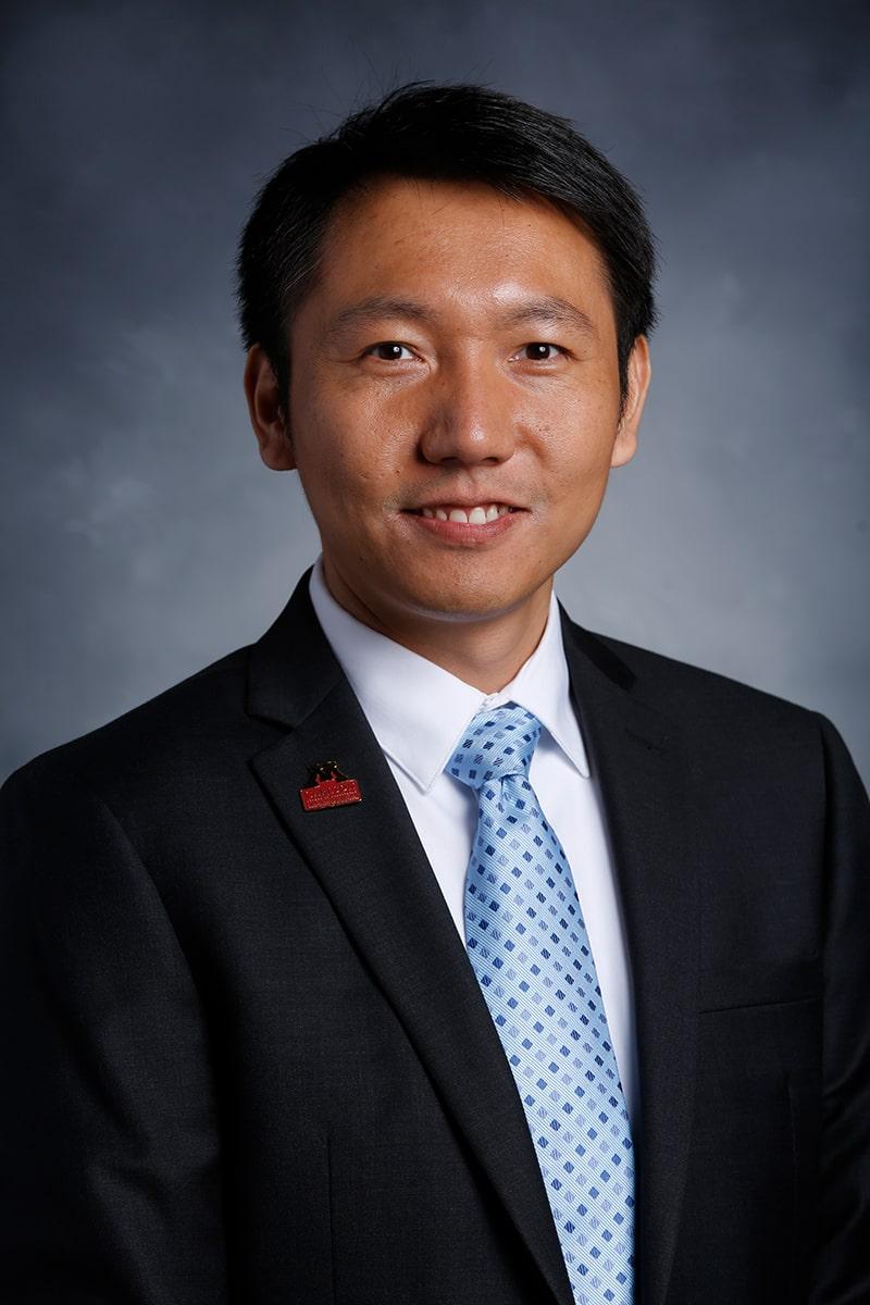 Stephen Xiang Li headshot photo in front of a blue and grey backdrop.