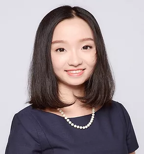 A photo of yiming Ma from the chest up, smiling at the camera. She is wearing a boat necked navy top or dress and a white pearl necklace.