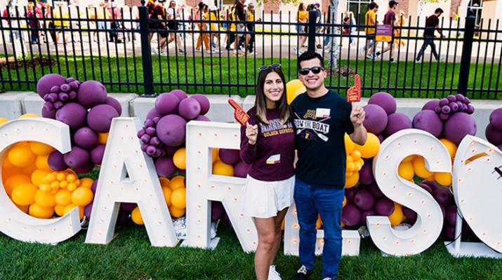 Two Carlson School alumni posing in front of Carlson block letters at a homecoming tailgate.