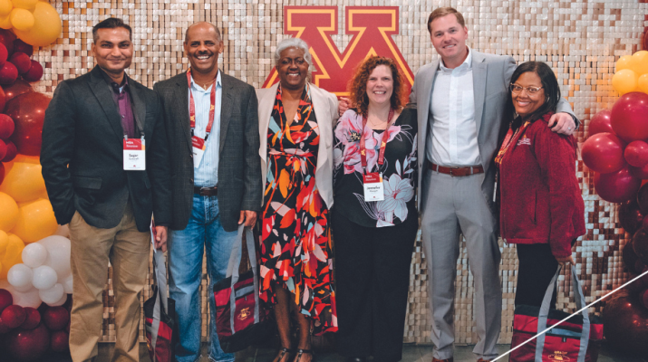 Group of MBA alumni posing in front of maroon and gold photo backdrop.