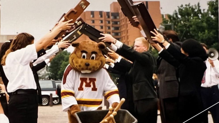 Goldy pushing through a wheelbarrow through a tunnel of briefcases at the 1995 Carlson School groundbreaking event. 