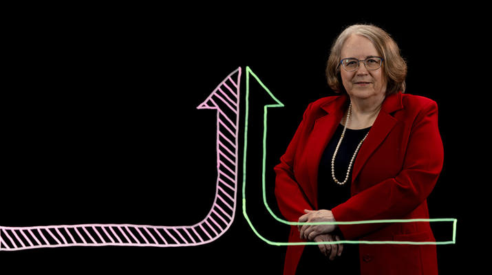 Deborah John stands behind an illustration of two different arrows coming together