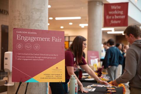 Engagement Fair sign next to a table with a career services staff sliding a sticker to a student. 