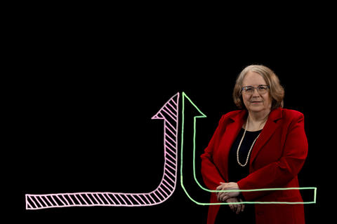 Deborah John stands behind an illustration of two different arrows coming together