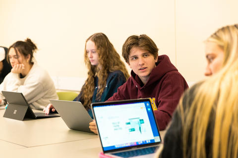 Four students sit at table with their laptops to discuss a project in the Carlson Impact Lab.