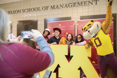 Class of 2023 graduates pose behind University block M logo with Goldy gopher.