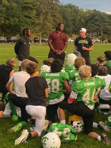 Gophers football players speaking to a group of young football players kneeling on the field.