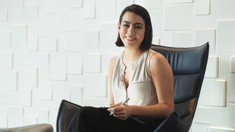 Business woman with tablet computer at work in office waiting room. Successful hispanic female manager sitting on armchair and smiling with confident expression