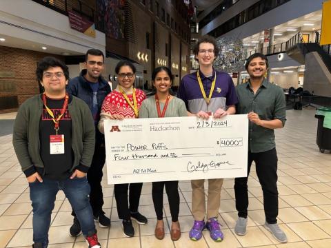 A team of six graduate students stand with an oversize $4,000 check to celebrate their win of the Hackathon.