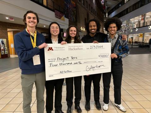 A team of five undergraduate students pose with an oversize $4,000 check to celebrate their win of the Hackathon.