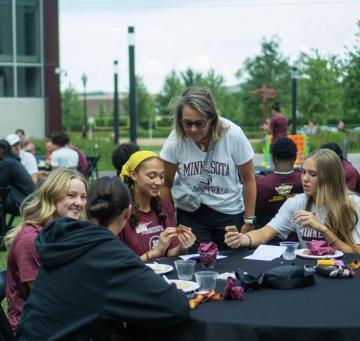 Gophers basketball player at a table with other students after a meal in a park.