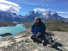 Stephen Drott sitting on flat rock with lake and mountain in background.