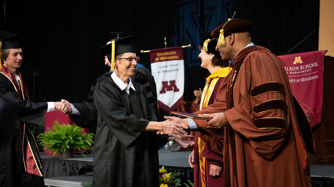 Graduate Kay Lacher shakes hands with Alok Gupta at the 2022 commencement ceremony