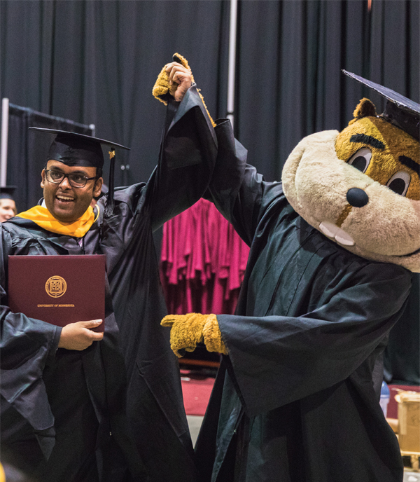 Goldy the Fopher holding a graduate's arm up at graduation